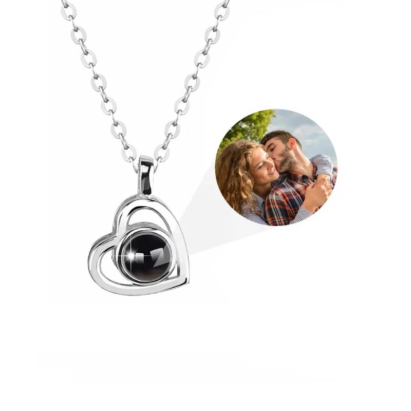 Heart-shaped silver pendant with a black stone on a white background, accompanied by a circular photo of a couple embracing.